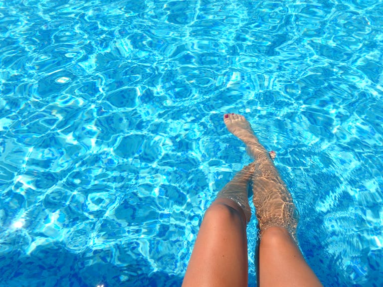 A person relaxes in a swimming pool with clear blue water, capturing summer vibes.