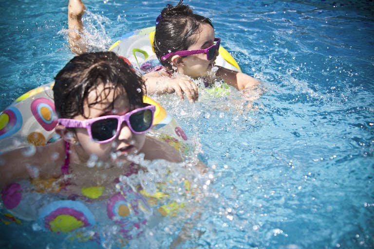 Two young girls enjoying a playful day in a bright blue swimming pool with colorful float rings.